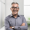 Smiling middle-aged man wearing glasses and a gray shirt with arms crossed.